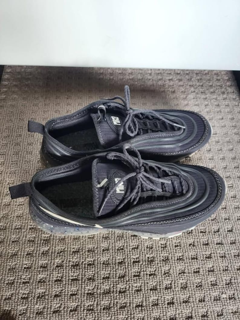 Puede incluir: Par de zapatillas deportivas negras con cordones. Las zapatillas tienen un dise&ntilde;o texturizado y una suela blanca con un patr&oacute;n moteado. Las zapatillas est&aacute;n sobre una superficie estampada.