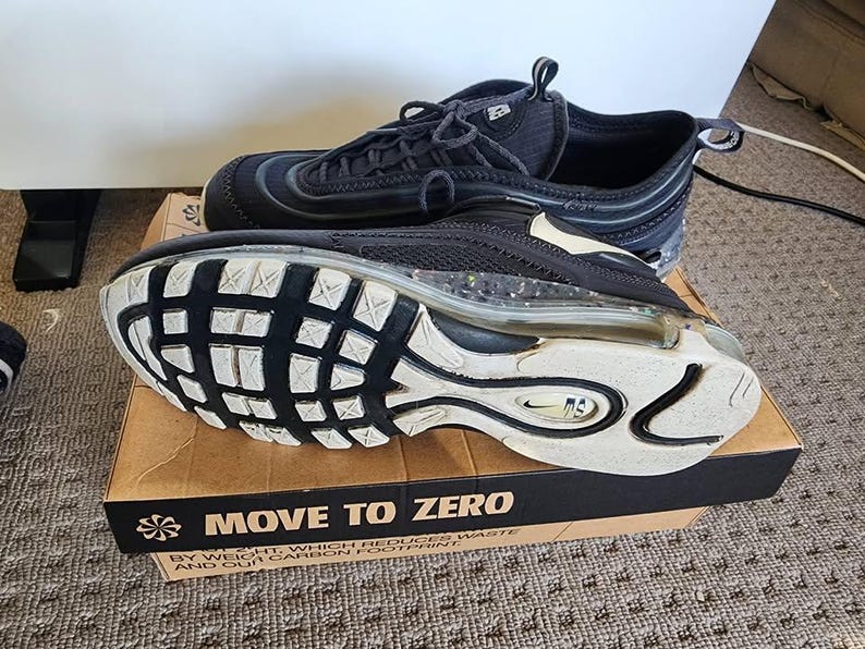 Puede incluir: Zapatillas deportivas negras con suelas blancas y una burbuja de aire visible. Las zapatillas est&aacute;n sobre una caja de cart&oacute;n con el texto "MOVE TO ZERO". Las zapatillas tienen cordones negros y un dise&ntilde;o de malla.