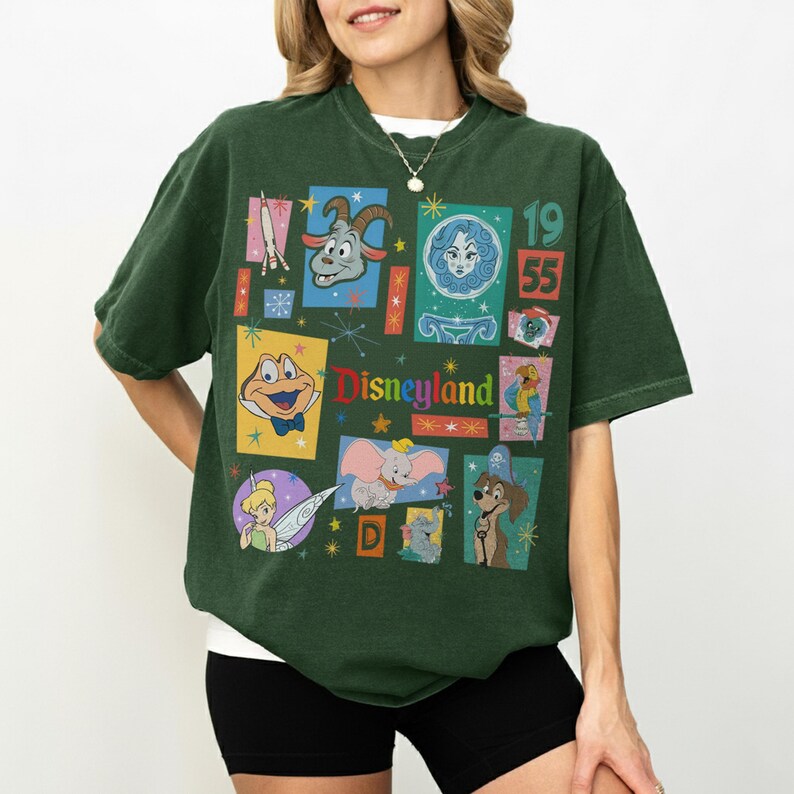 K&ouml;nnte beinhalten: Dunkelgr&uuml;nes T-Shirt mit einem Vintage-Disneyland-Collage-Design. Das Design zeigt verschiedene Charaktere, das Disneyland-Logo und das Jahr 1955. Das Shirt hat eine lockere Passform und kurze &Auml;rmel.