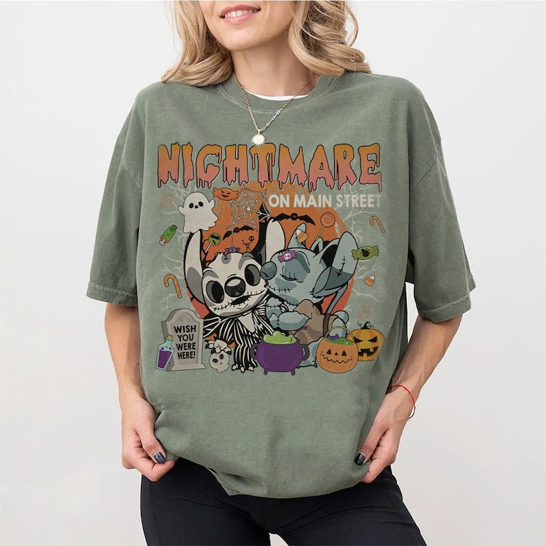 Puede incluir: Camiseta verde oliva con un dise&ntilde;o de Halloween. El dise&ntilde;o presenta el texto "Nightmare on Main Street" y personajes de dibujos animados, calabazas, un fantasma y una l&aacute;pida que dice "Wish You Were Here!"