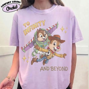 May include: A light purple t-shirt featuring a graphic of two chipmunks dressed as space and cowboy characters. One chipmunk wears a space suit with wings, and the other wears a cowboy hat and vest. The text reads TO INFINITY AND BEYOND.