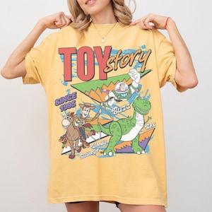 May include: Mustard yellow t-shirt with a Toy Story graphic. The design features Woody, Buzz Lightyear, and Rex, with the text "TOY Story" and "SINCE 1995". The shirt has a vintage, slightly faded appearance.