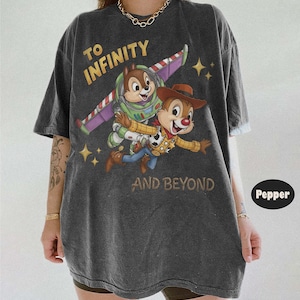 May include: A charcoal grey short-sleeve t-shirt featuring a graphic of two chipmunks dressed as space and cowboy characters. The text reads TO INFINITY AND BEYOND. The shirt has a faded, washed-out appearance with a crew neckline and loose fit.