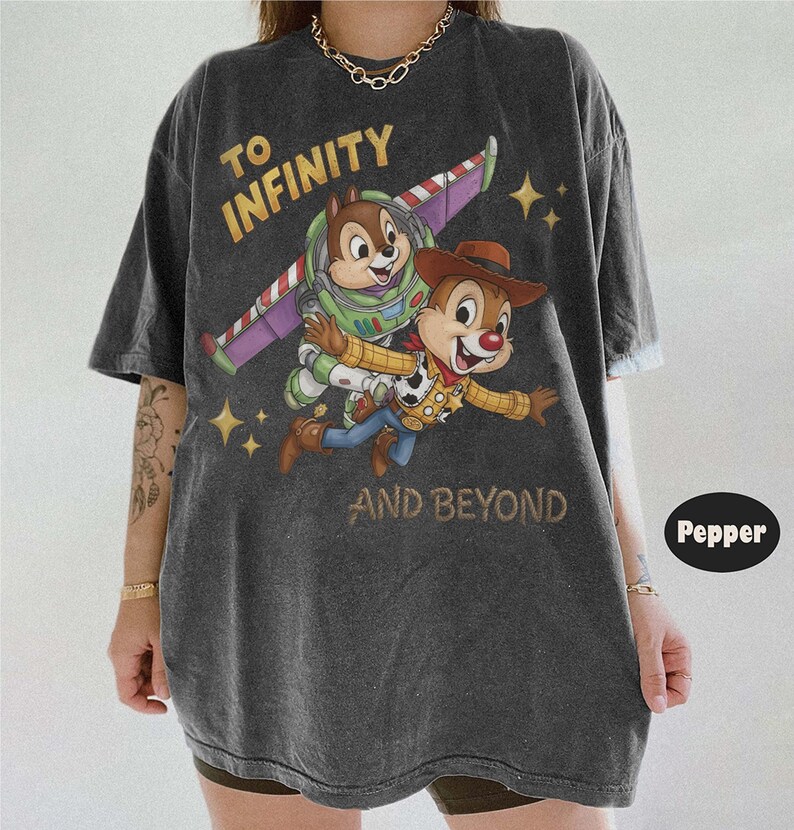 May include: A charcoal grey short-sleeve t-shirt featuring a graphic of two chipmunks dressed as space and cowboy characters. The text reads TO INFINITY AND BEYOND. The shirt has a faded, washed-out appearance with a crew neckline and loose fit.