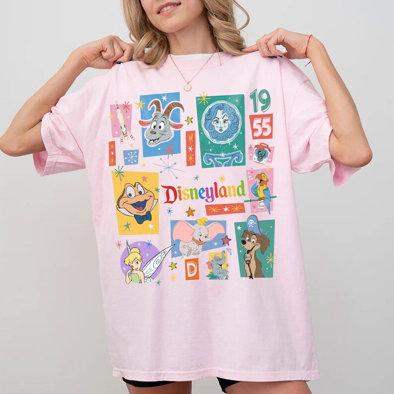 K&ouml;nnte beinhalten: Hellrosa T-Shirt mit farbenfrohem Disneyland-Motiv. Das Motiv zeigt verschiedene Disney-Figuren sowie den Schriftzug "Disneyland" und die Zahlen "1955". Das T-Shirt hat kurze &Auml;rmel und eine lockere Passform.