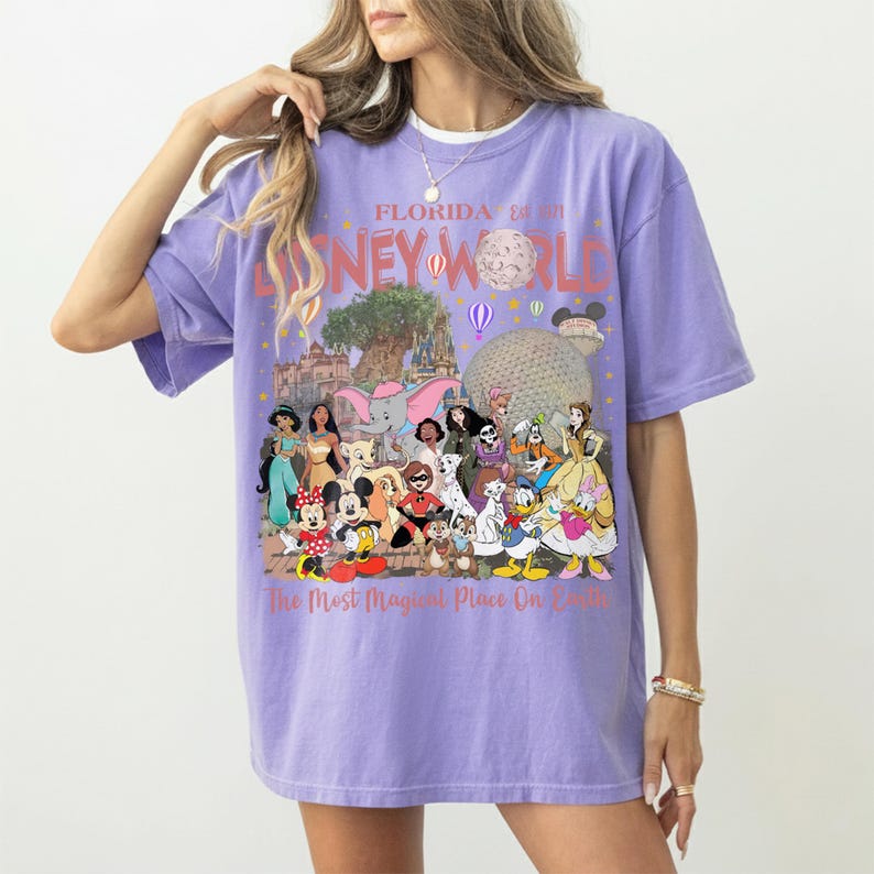 May include: A lilac-colored t-shirt featuring a colorful graphic of Disney World characters and landmarks. The text "Florida Disney World" and "The Most Magical Place On Earth" are printed on the shirt.