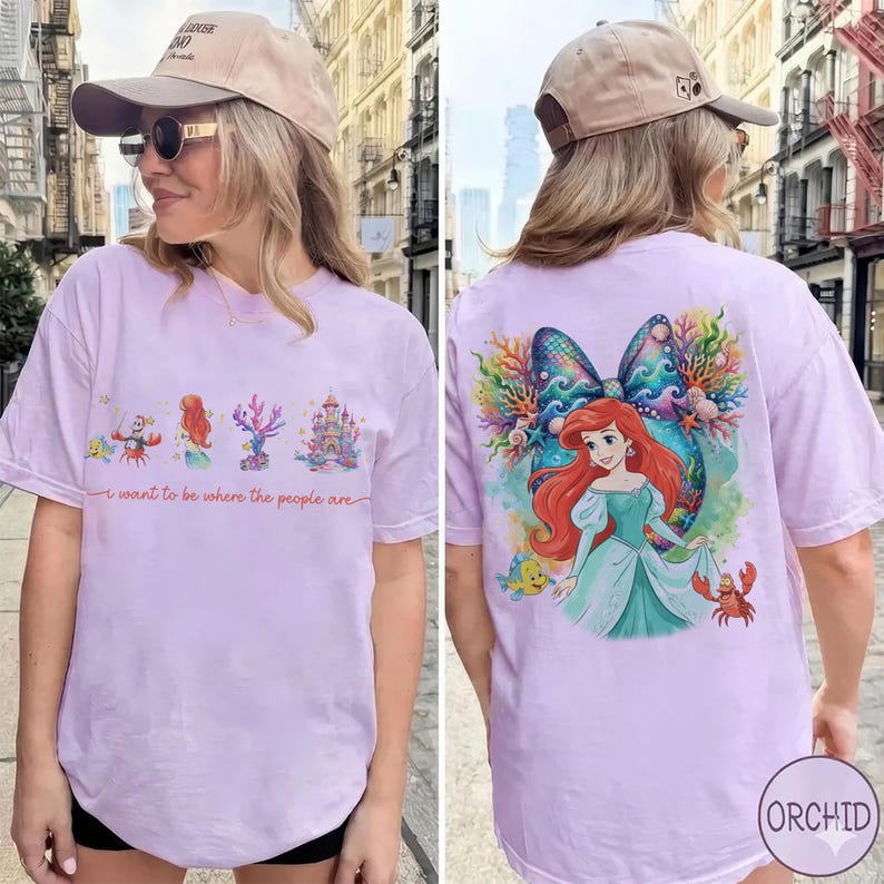 May include: Lilac t-shirt featuring a front graphic with Ariel and other characters from The Little Mermaid, along with the text "I want to be where the people are." The back of the shirt has a larger Ariel graphic.
