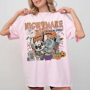 Puede incluir: Camiseta rosa claro con un dise&ntilde;o tem&aacute;tico de Halloween. El dise&ntilde;o incluye las palabras "NIGHTMARE ON MAIN STREET" en naranja, junto con personajes de dibujos animados, calabazas y una l&aacute;pida que dice "WISH YOU WERE HERE!"