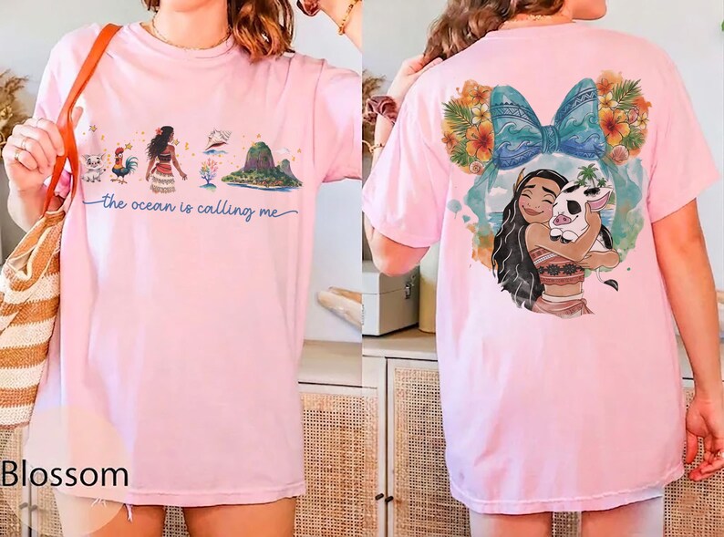 May include: Light pink t-shirt featuring a colorful graphic of a cartoon character and the text "the ocean is calling me". The back of the shirt has a graphic of the same character hugging a pig. The shirt is a casual style.