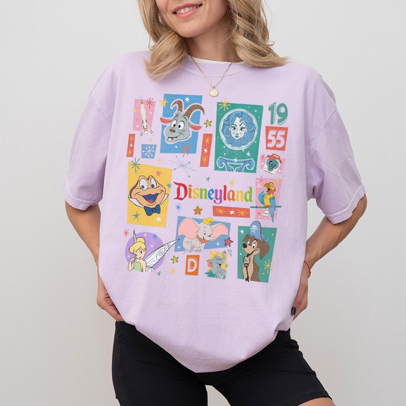 K&ouml;nnte beinhalten: Ein helllila T-Shirt mit einer farbenfrohen Collage von Disney-Figuren und dem Wort "Disneyland". Das Design enth&auml;lt Bilder von Dumbo, Tinkerbell und anderen klassischen Figuren, mit dem Jahr 1955 prominent dargestellt.