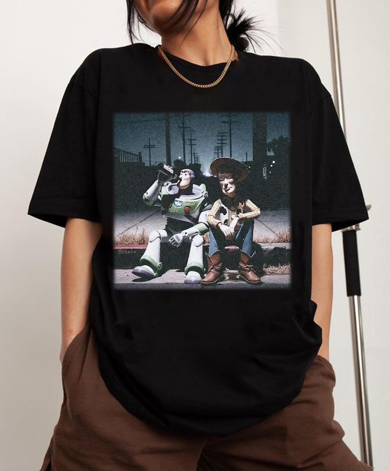 Puede incluir: Camiseta negra con un gr&aacute;fico de Buzz Lightyear y Woody de Toy Story sentados juntos. Buzz est&aacute; bebiendo de una lata. La imagen tiene un aspecto vintage, ligeramente desgastado.