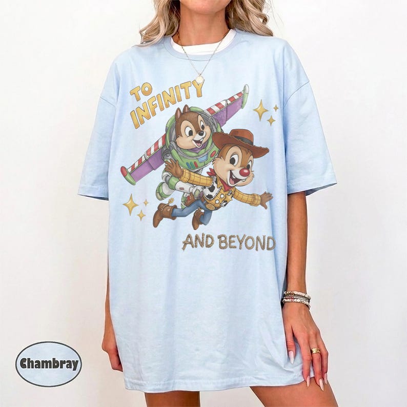 May include: A light blue t-shirt featuring a graphic of two chipmunks dressed as space and cowboy characters flying through the air. The text reads TO INFINITY AND BEYOND. A small circular label in the corner displays the word Chambray.