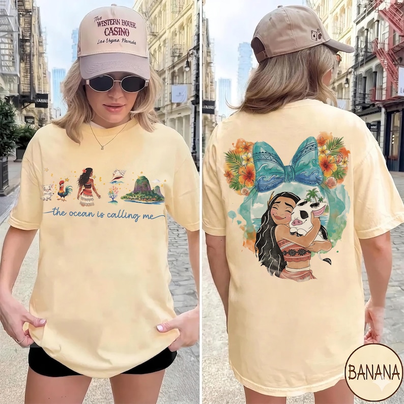 May include: A light yellow t-shirt featuring a graphic of a cartoon character with a pig, surrounded by flowers and a blue bow. The front of the shirt has a graphic of a cartoon character and the text "the ocean is calling me".