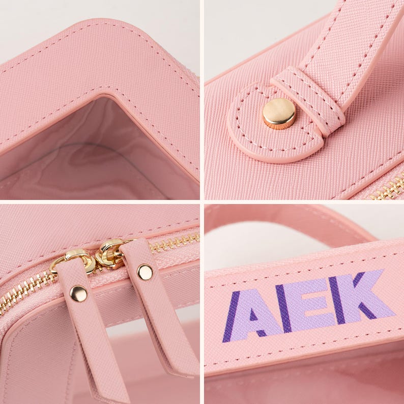 May include: A pink cosmetic bag with a clear window and gold-colored zipper. The bag has a handle with the letters "AEK" in purple. The bag is made of a textured material.