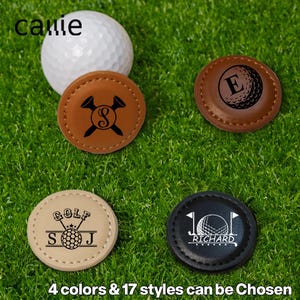 May include: A white golf ball sits on green grass with four personalised golf ball markers. The markers are brown, tan, and black, each with a unique design, including initials, a golf ball graphic, and the word "GOLF". The text "4 colors & 17 styles can be Chosen" is at the bottom.
