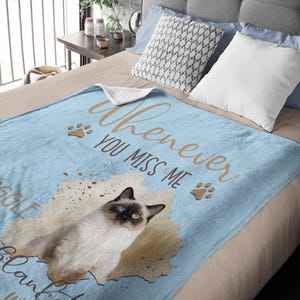 K&ouml;nnte beinhalten: Hellblaue Decke mit einer Siamkatzen-Illustration und dem Text "Whenever you miss me". Die Decke hat eine weiche Textur und Pfotenabdr&uuml;cke. Die Katze hat blaue Augen und ein braun-wei&szlig;es Fell.