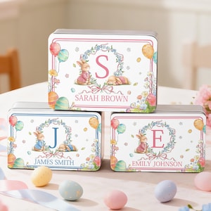 May include: Three personalized Easter-themed metal tins. Each tin features a bunny illustration, floral wreath, balloons, and Easter eggs. The top tin reads "Sarah Brown", the middle tin reads "James Smith", and the bottom tin reads "Emily Johnson".