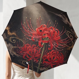 Pode incluir: Um guarda-chuva preto com uma estampa vibrante de lírios-aranha vermelhos com gotas de água. O design inclui detalhes de linhas douradas fluidas sobre um fundo escuro, com as flores exibidas em um estilo artístico detalhado e realista.