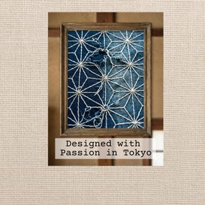 以下が含まれることがあります： 藍染めの生地に白い幾何学模様のステッチが施された額装作品。木製のフレームに入っており、下部には「Designed with Passion in Tokyo」の文字が書かれています。