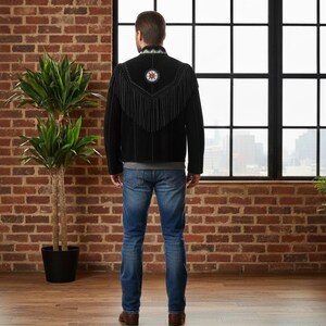 May include: A black jacket featuring long fringe detailing across the back and shoulders, a high collar with intricate beadwork, and a circular beaded emblem centred on the upper back, paired with blue denim jeans.