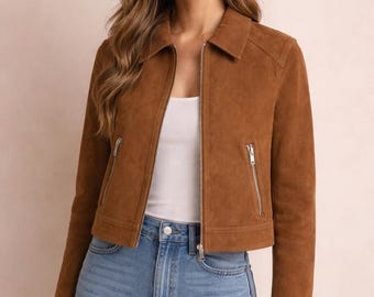 May include: A brown suede jacket featuring a classic collar, a full-length silver-tone front zip, and two vertical zipped pockets on the front. The jacket is worn over a plain white top and light blue denim jeans, showcasing a clean design.