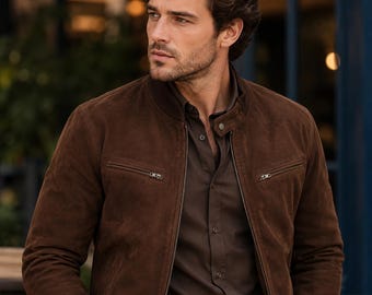 May include: A dark brown suede bomber jacket featuring a stand-up collar with a snap button closure, a full-length front zip, and two horizontal zipped chest pockets. The jacket is worn over a dark brown button-down shirt with a pointed collar.