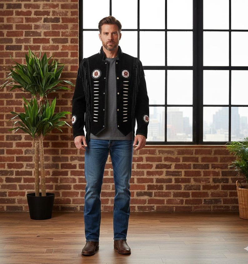 May include: A black suede jacket featuring long fringe along the sleeves and chest, accented with white leather lacing and circular beaded medallions on the chest and sleeves. The jacket is worn over a grey t-shirt and blue denim jeans.