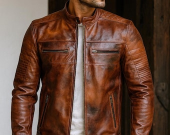 May include: A brown leather jacket with a distressed finish, featuring a mandarin collar, a full-length front zip, two horizontal zipped chest pockets, two lower zipped pockets, and quilted shoulder detailing over a white shirt.