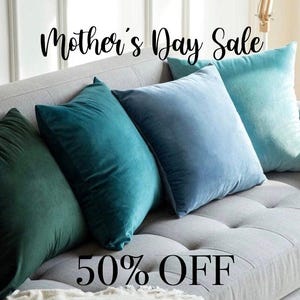 May include: A collection of four square throw pillows in shades of teal and blue arranged on a gray sofa. The pillows have a soft, velvety texture. The words "Mother's Day Sale" and "50% OFF" are displayed in black script.