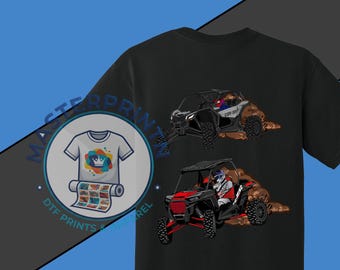 May include: Black t-shirt featuring two off-road vehicles kicking up dirt. The vehicles are black, red, and white. A logo with a t-shirt design is on the left side of the shirt. The logo includes the text "DTF PRINTS APPAREL".