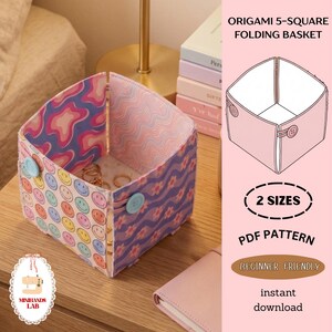 May include: A square origami folding basket with a colorful design. The basket features a smiley face pattern on one side and a floral pattern on the other. It is held together with two light blue buttons. The image also includes text that says "Origami 5-Square Folding Basket".