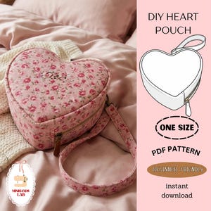 May include: A heart-shaped pouch with a floral pattern in pink and red. The pouch has a zipper closure, a brown leather pull, and a matching strap. The image also includes a diagram of the pouch and text that says "DIY HEART POUCH", "ONE SIZE", "PDF PATTERN", and "BEGINNER FRIENDLY".