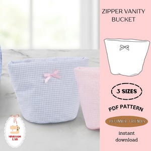 May include: Two fabric vanity buckets, one light blue gingham and one pink, are displayed. Each has a small pink bow. The image includes text that reads "ZIPPER VANITY BUCKET", "3 SIZES", "PDF PATTERN", and "BEGINNER FRIENDLY".