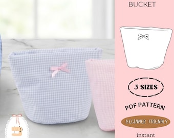 Peut inclure: Deux seaux de vanité en tissu, un à carreaux vichy bleu clair et un rose, sont présentés. Chacun a un petit nœud rose. L'image comprend le texte "ZIPPER VANITY BUCKET", "3 SIZES", "PDF PATTERN" et "BEGINNER FRIENDLY".