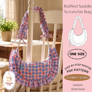 Op de afbeelding: Een roze zadeltas met een blauwe appel- en rode kersenprint, voorzien van een geplooide rand en een geplooide schouderband in scrunchie-stijl met kleine strikjes. De tekst luidt Ruffled Saddle Scrunchie Bag, One Size, Step By Step Photos PDF Pattern.
