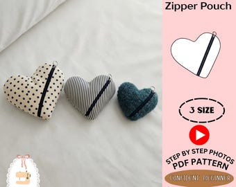 Peut inclure: Trois pochettes zippées en forme de cœur de différentes tailles et tissus : une crème à pois noirs, une à rayures verticales grises et blanches, et une en tissu bleu sarcelle texturé. Chacune possède une fermeture éclair noire et un anneau.