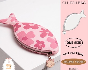Peut inclure: Pochette rose en forme de poisson avec un motif floral et une fermeture éclair. Un charm en forme de chat est attaché à la fermeture éclair. Le texte comprend "DIY FISH CLUTCH BAG", "ONE SIZE", "PDF PATTERN", "BEGINNER FRIENDLY", et "instant download".