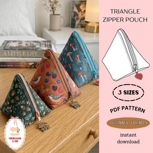 May include: Three triangle-shaped zipper pouches with nature-themed patterns. One is green with acorns, another is orange with birds and berries, and the third is blue with mushrooms. The pouches have metal zipper pulls and are displayed on a wooden surface.