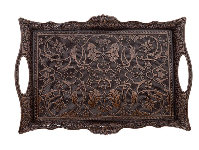 Pode incluir: Bandeja retangular decorativa marrom escuro com um intrincado padr&atilde;o floral e de folhas. A bandeja apresenta uma superf&iacute;cie texturizada e al&ccedil;as integradas. As bordas e as al&ccedil;as t&ecirc;m um design detalhado em relevo. Uma pe&ccedil;a decorativa.