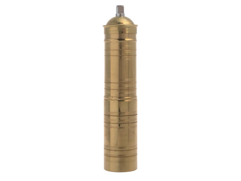 May include: A tall, brass-colored pepper mill with a cylindrical body. The mill features horizontal etched bands and a textured top and bottom. The top has a small, square-shaped metal piece. The pepper mill is designed for grinding spices.