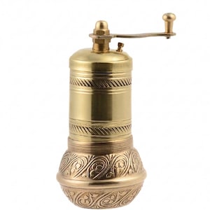 May include: A brass pepper mill with a hand crank. The mill has a cylindrical body with decorative bands and an ornate, patterned base. The crank and top are also brass, creating a cohesive, vintage aesthetic.