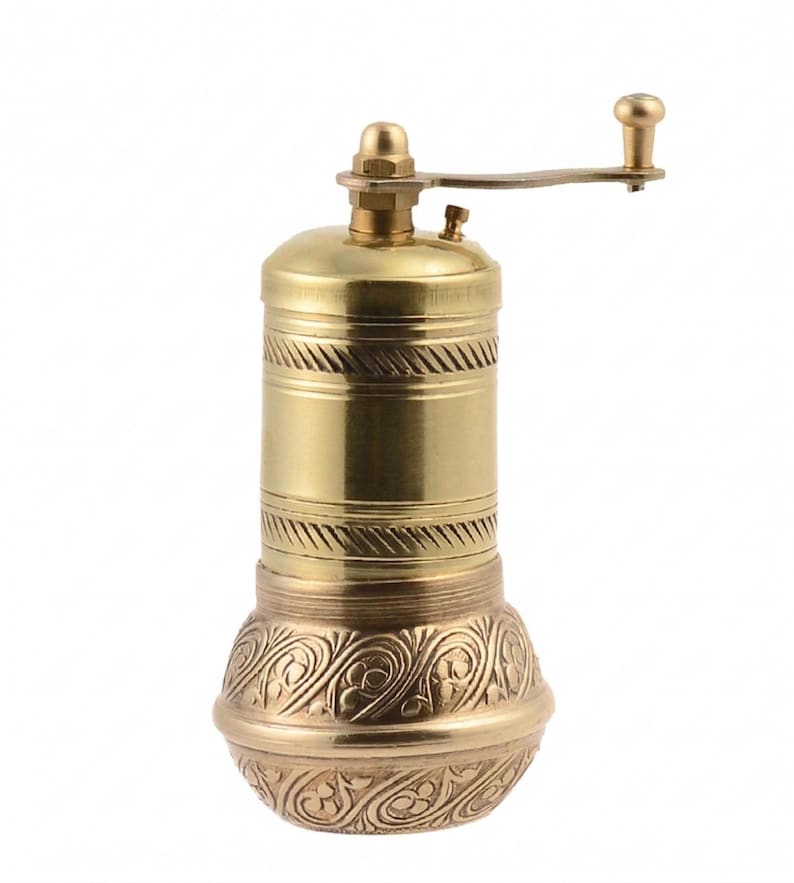 May include: A brass pepper mill with a hand crank. The mill has a cylindrical body with decorative bands and an ornate, patterned base. The crank and top are also brass, creating a cohesive, vintage aesthetic.