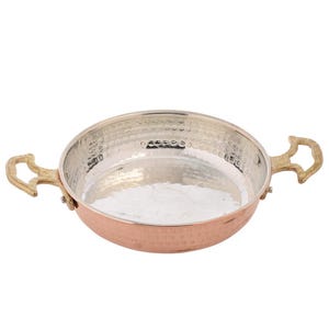 Puede incluir: Una sart&eacute;n de color cobre, con acabado martillado, interior plateado y dos asas de lat&oacute;n. La sart&eacute;n tiene forma redonda y poco profunda, adecuada para cocinar y servir. Las asas son curvas y decorativas.