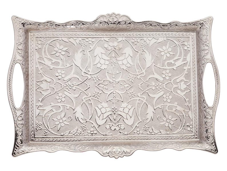 Pode incluir: Uma bandeja de servir prateada retangular com padr&otilde;es florais e de folhas ornamentados. A bandeja tem al&ccedil;as curvas em cada lado e uma borda decorativa ondulada. A superf&iacute;cie &eacute; coberta por um design detalhado em relevo.