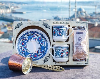 May include: A Turkish coffee set includes two small mugs, a saucer, and a bag of coffee, all presented in a wooden box. The mugs and saucer feature a blue and red floral design. A copper coffee pot and a decorative spoon are also included.