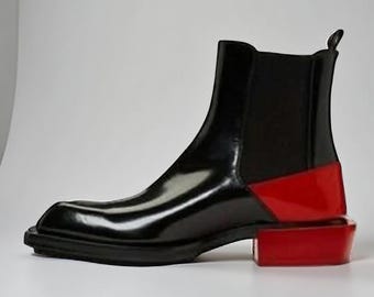 May include: A black ankle boot with a square toe and a red block heel. The boot has a glossy finish and elastic side panels. The heel measures approximately 5 cm.
