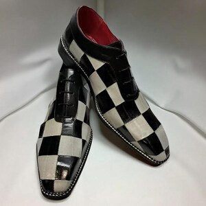 Op de afbeelding: Een paar zwart-wit geblokte geklede schoenen met zwarte veters. De schoenen hebben een glanzende afwerking op de zwarte vierkanten en een matte afwerking op de witte vierkanten. De binnenvoering is rood.