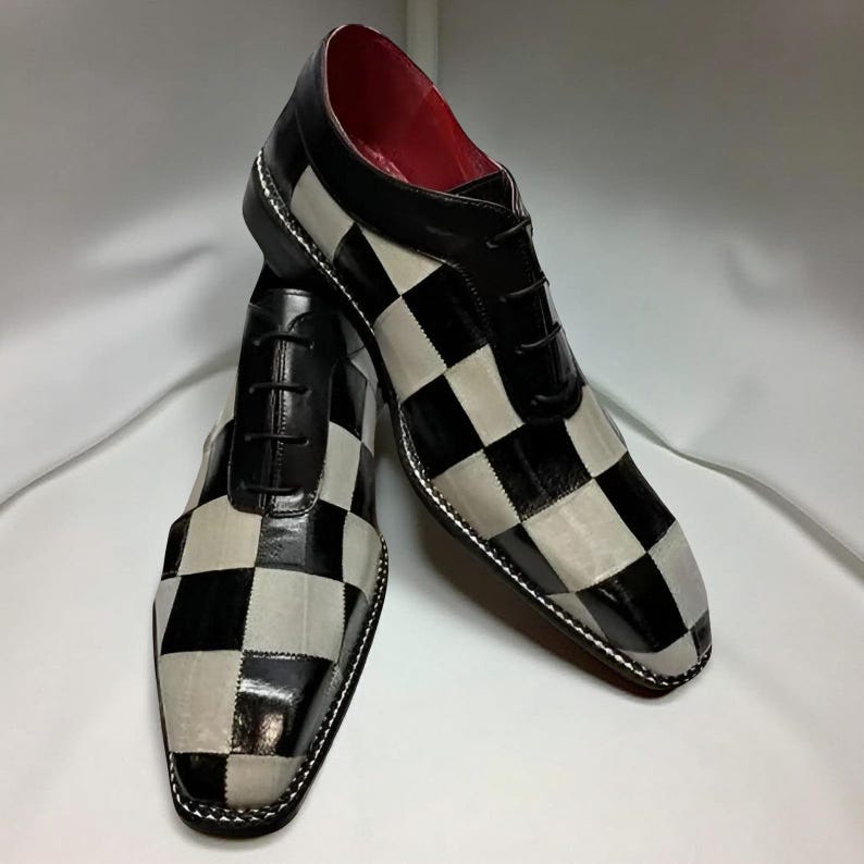 Op de afbeelding: Een paar zwart-wit geblokte geklede schoenen met zwarte veters. De schoenen hebben een glanzende afwerking op de zwarte vierkanten en een matte afwerking op de witte vierkanten. De binnenvoering is rood.