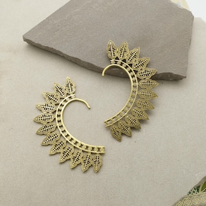 May include: Two gold-colored ear cuffs, each featuring a leaf design. The leaves are arranged in a semi-circular pattern around the ear, with a curved hook for secure placement. The intricate design adds a touch of elegance.