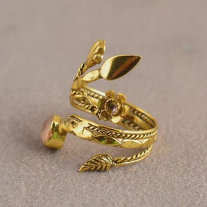 Peut inclure: Une bague dor&eacute;e r&eacute;glable avec un motif floral et de feuilles. La bague pr&eacute;sente une pierre pr&eacute;cieuse rose et est fabriqu&eacute;e en forme de spirale. La conception de la bague comprend des fleurs et des feuilles.